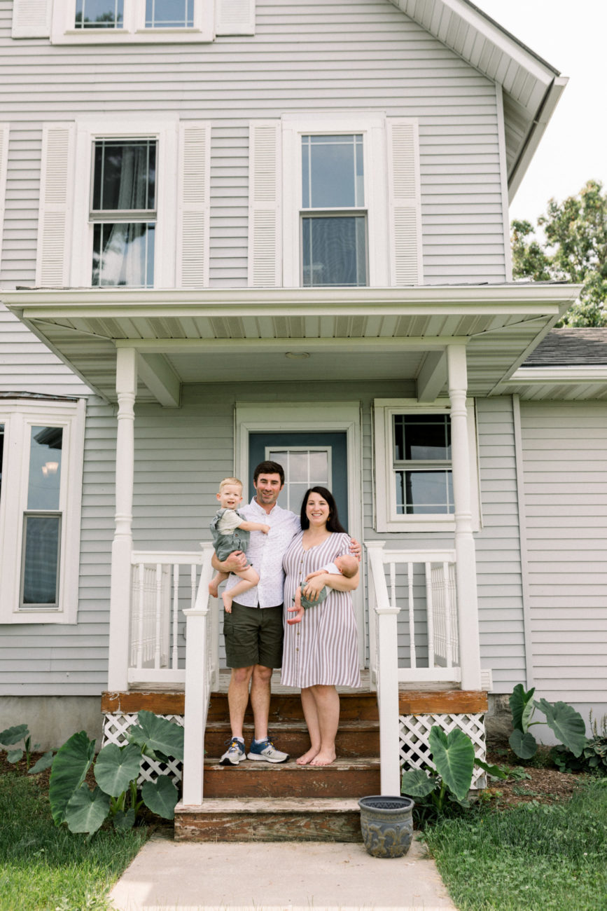 Family standing outside of farm house in Iowa with new baby